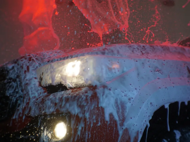 Thick pre-soak foam covering a car under the wash tunnel lights