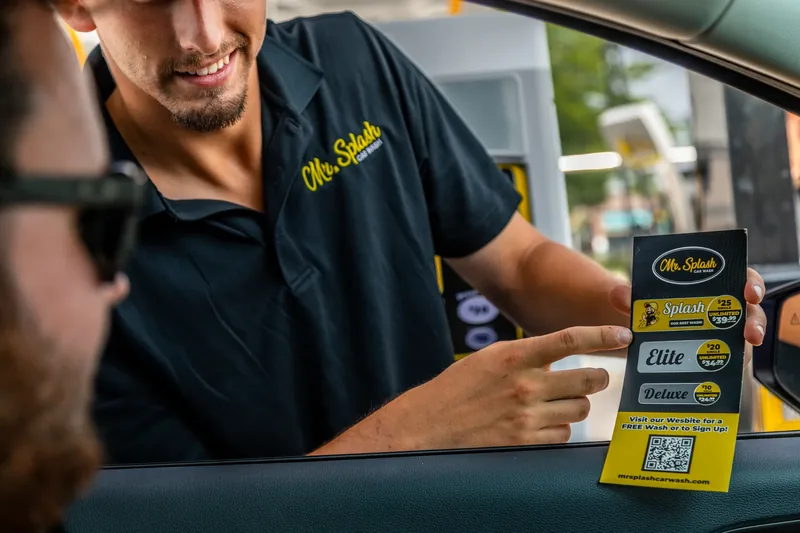A Mr. Splash team member showing the wash menu to a customer at the pay station
